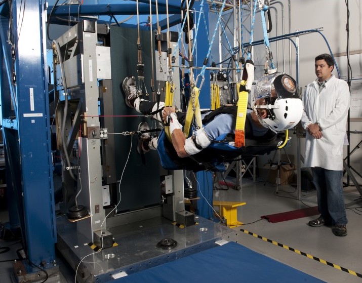 Researchers watch a person suspended horizontal to the ground by straps walk on a vertical treadmill.