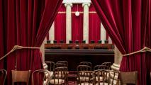 View of a courtroom through parted red curtains, revealing wooden chairs and a judge's bench flanked by large pillars, reminiscent of the grandeur often seen in images of the Supreme Court shared on social media.