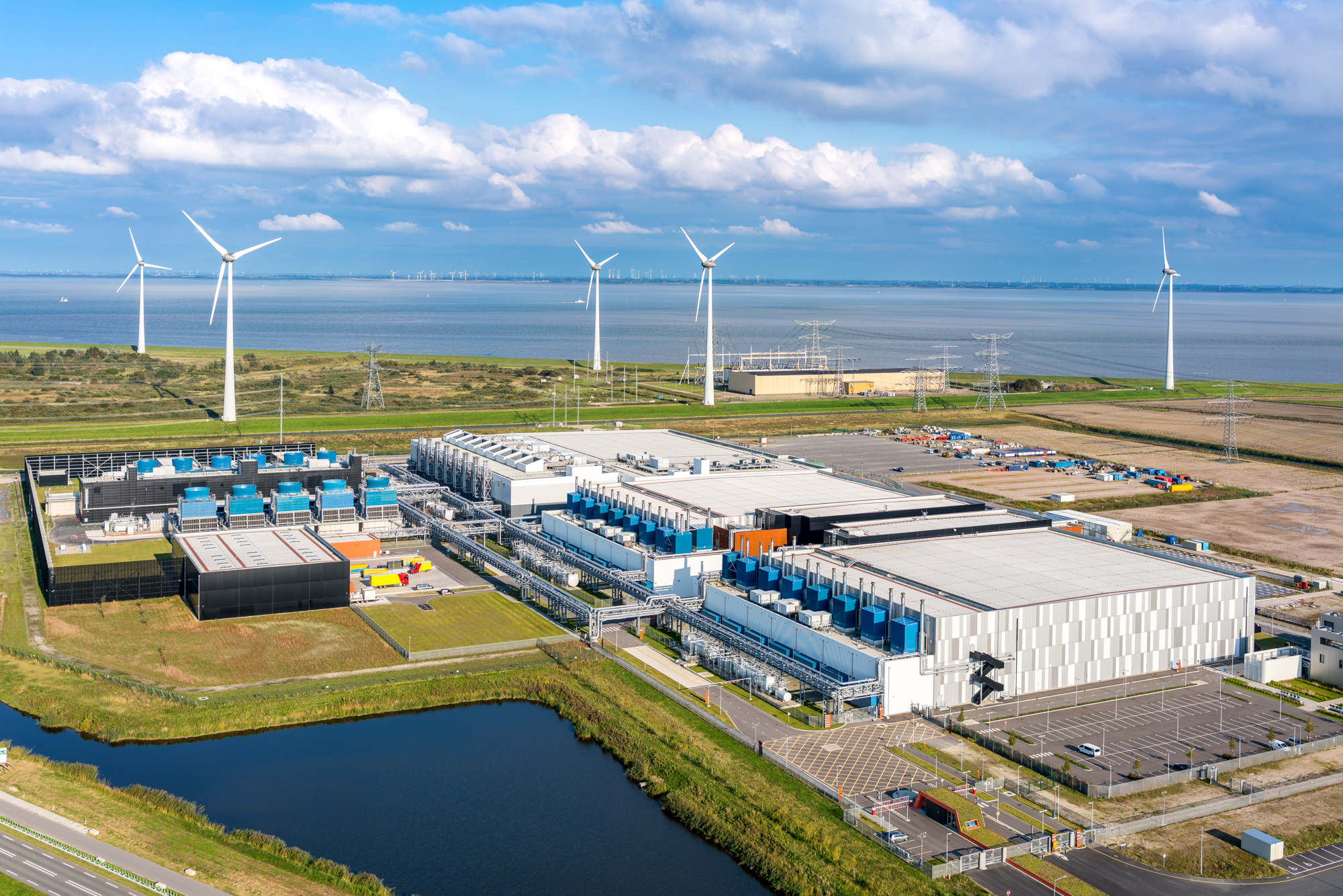 an aerial image of a large building with wind turbines and a body of water in the background