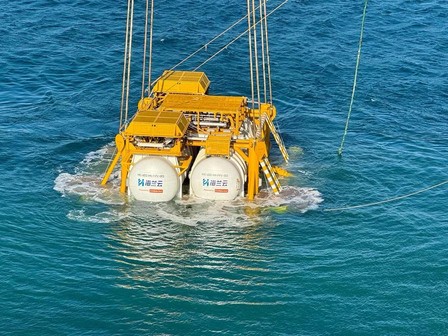 A large yellow and white submersible device with Chinese text is being lowered into the ocean using several cables.