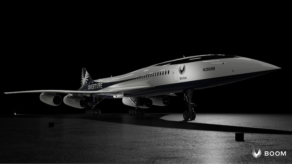 A sleek, futuristic aircraft with the word "Overture" on its side sits in a dimly lit hangar, showcasing Boom branding. It's a marvel of supersonic flight engineering.