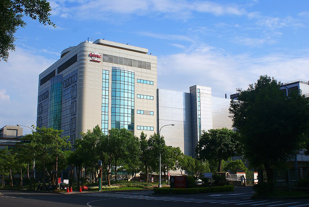 Modern office building with reflective glass windows surrounded by trees under a blue sky.