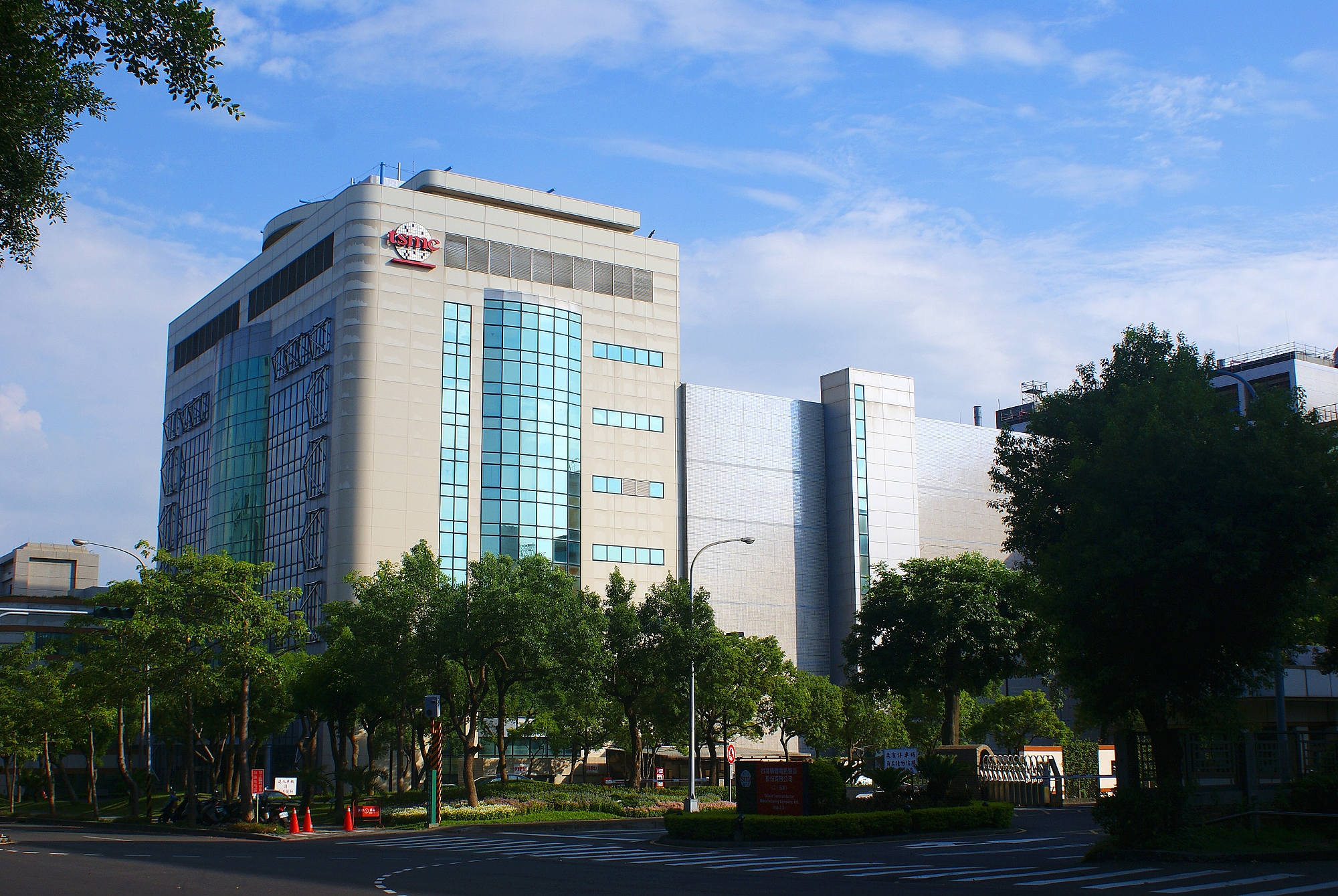 Modern multistory office building with reflective glass windows, surrounded by trees, under a clear blue sky.