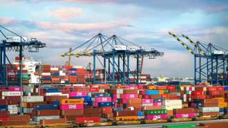 Cargo containers stacked at a bustling port, where massive cranes tower under a cloudy sky, streamline the shipping process with precision akin to generative AI's innovative efficiency.