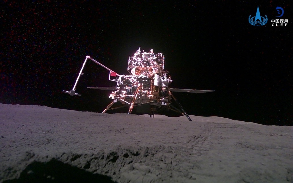 Lunar lander on the moon's surface with a robotic arm extended, under a dark sky.