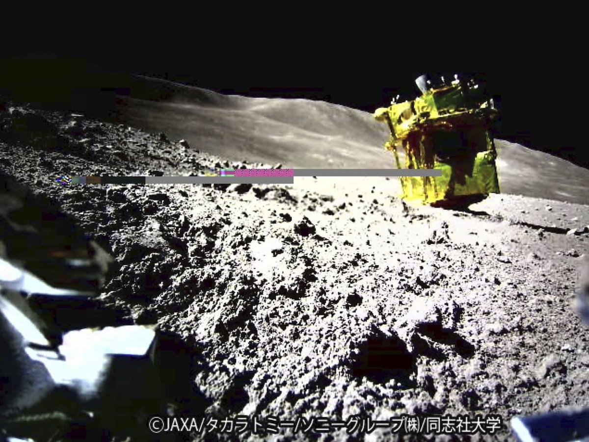 A space probe is landed on the rocky surface of an asteroid, with sunlight casting shadows.