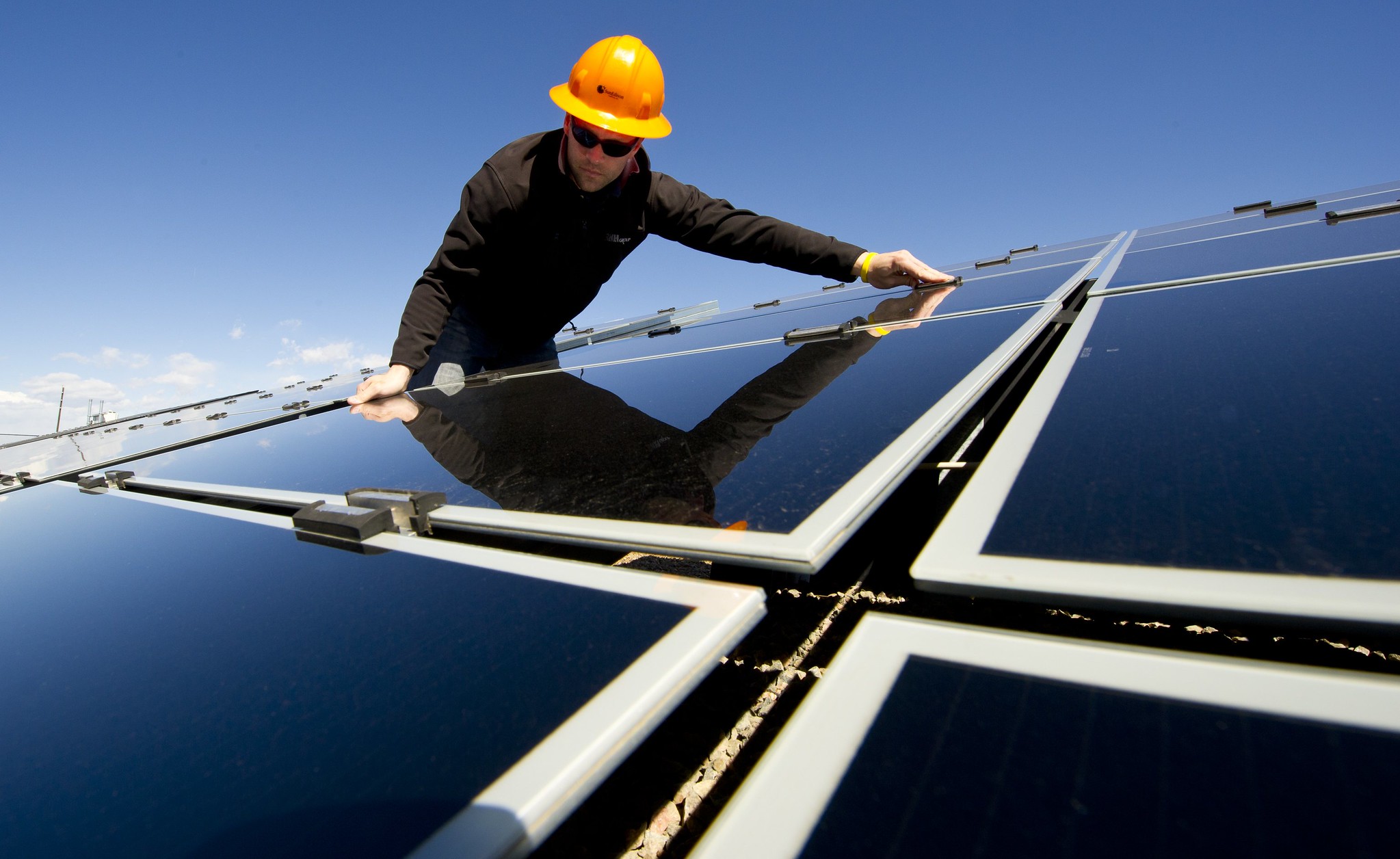 A worker in a hard hat adjusts solar panels under a clear blue sky, contributing to the growing field of green jobs.